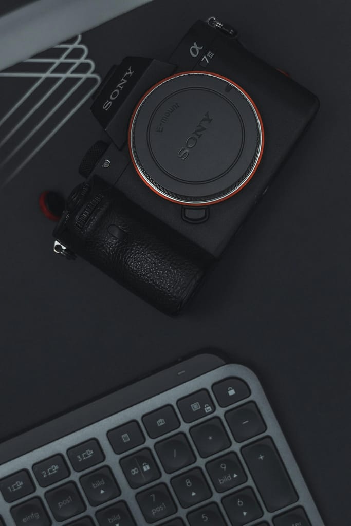 Flat lay of a camera and keyboard on a dark surface, emphasizing technology and modern design.
